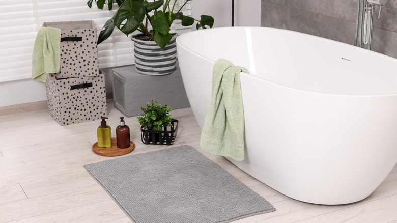 bathroom with free standing bath tub, a grey bathroom mat , products, bath towels and plants