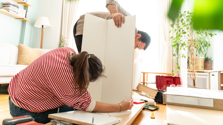 Couple assembling a white laminate piece of furniture in their living room