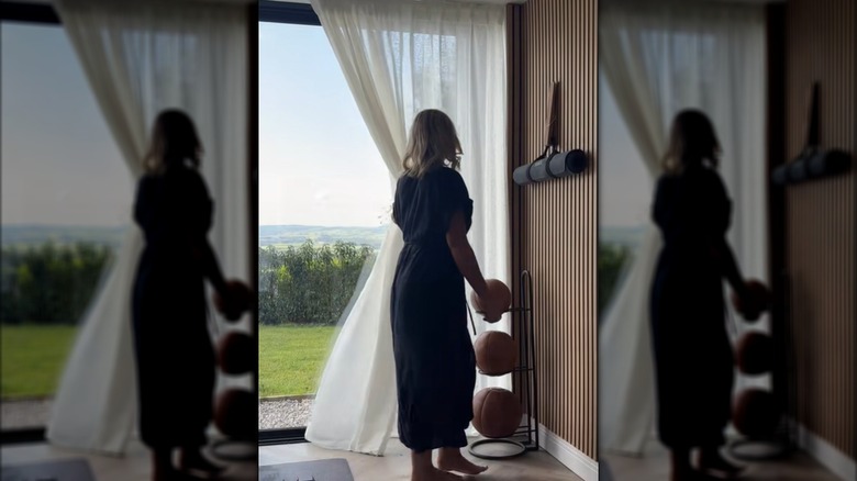 A woman slides open a sheer IKEA curtain on a wall of glass doors.