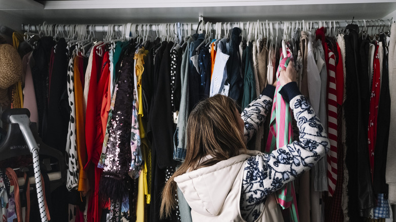 Person hanging up clothes in a cluttered closet