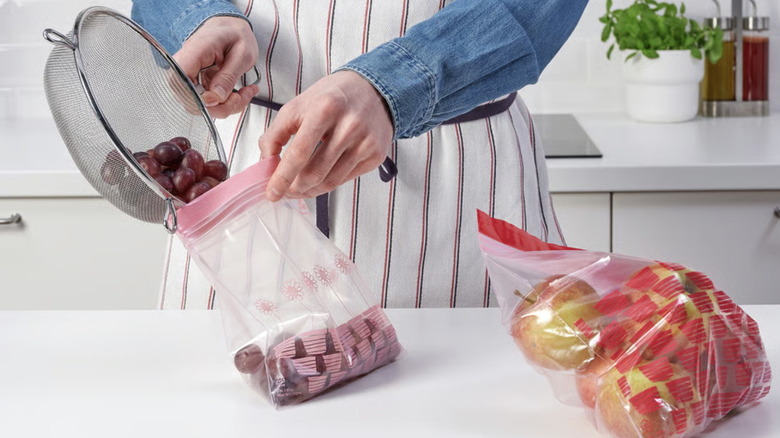 A person fills an IKEA ISTAD bag with grapes next to an ISTAD bag of apples