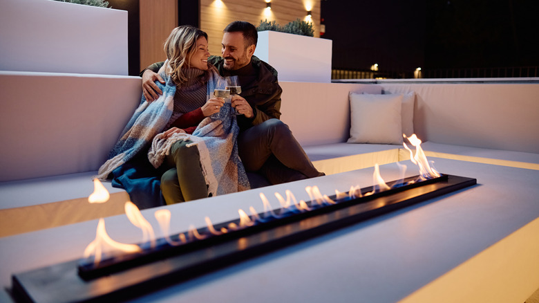A happy couple on a patio enjoying the warmth from a built-in fire pit