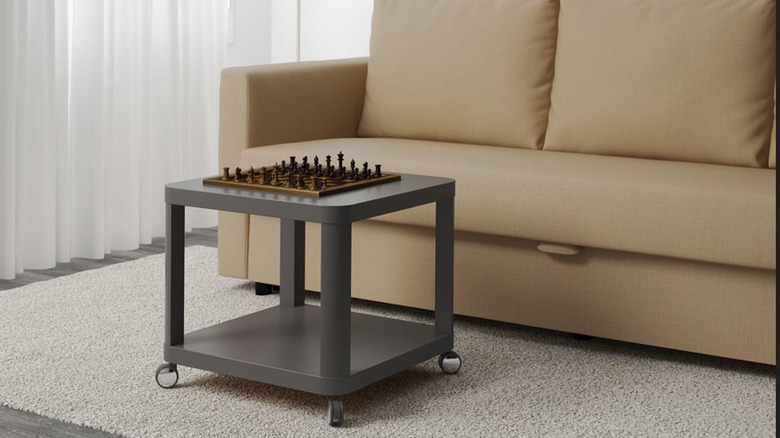 A dark gray TINGBY in front of a beige couch with a chess set on top