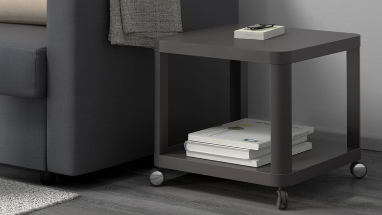 A dark gray TINGBY beside a dark gray couch with glasses, and several books on the shelves