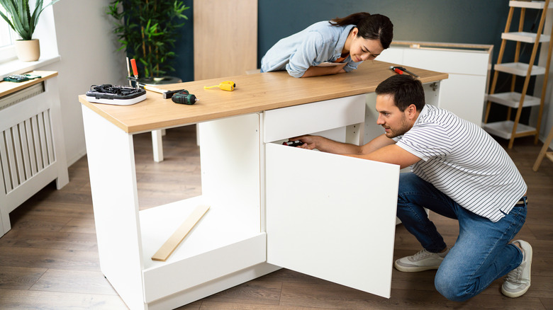 A couple installing the bottom of a kitchen cabinet with a wood top