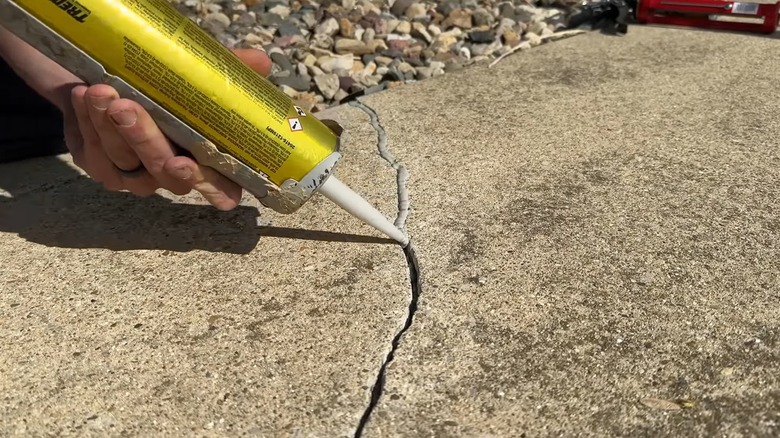 Person filling crack in concrete with filler