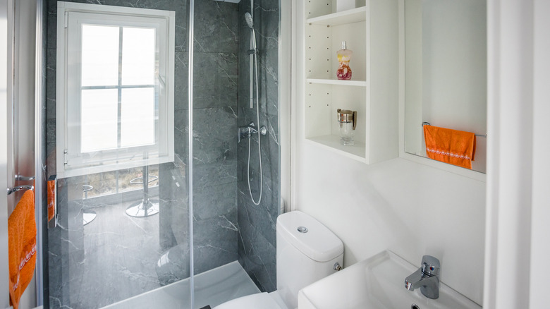 A white bathroom with a gray shower and orange accent towels