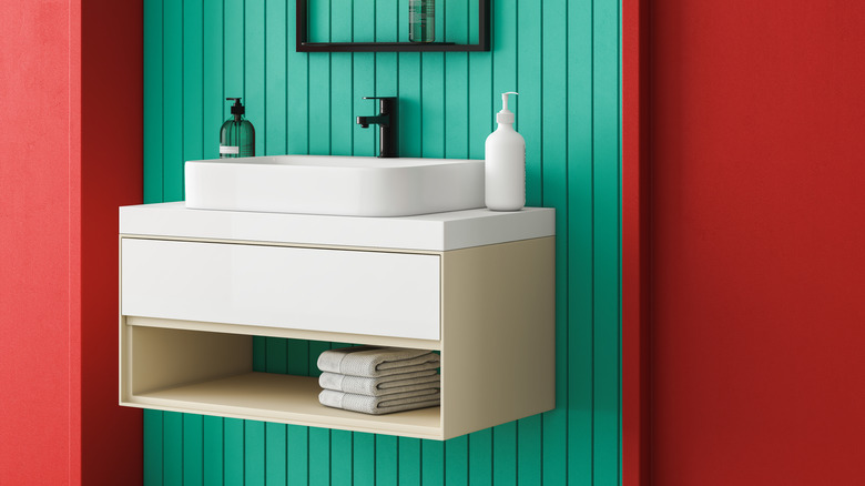 A white bathroom sink against a teal accent wall between red panels