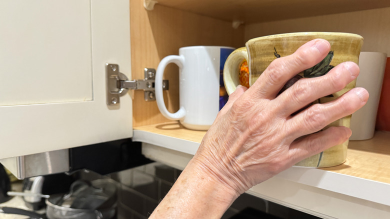 A hand grabbing a coffee mug out of the cabinet.