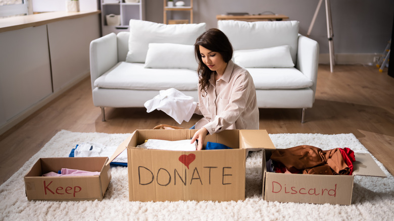 Woman in front of a white couch sorting items donate, keep, and discard boxes on a fluffy white rug