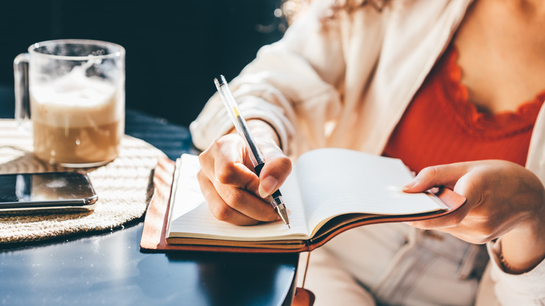 Woman sits with a coffee writing in a journal