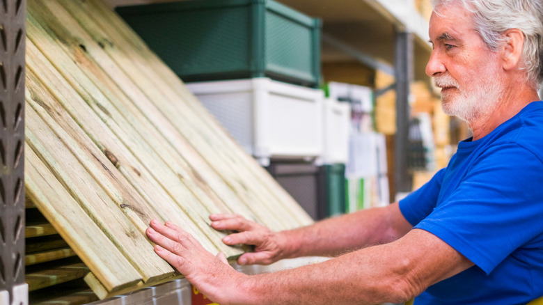 A older adult pulls a new wood pallet down from a shelf in a hardware store.
