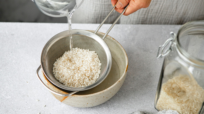 Woman rinsing white rice in a bowl with a strainer