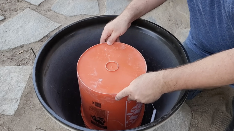 A man places an upturned orange Home Depot bucket inside a large planter.