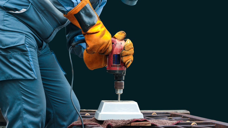 Someone drilling a hole into a small ceramic pot with safety equipment