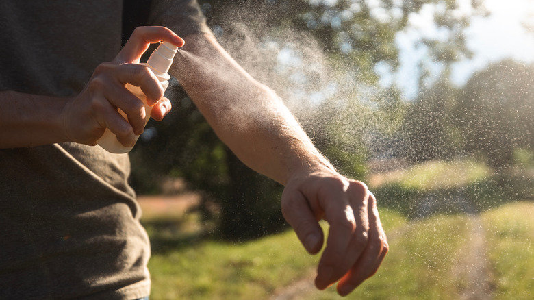 A person sprays bug spray on their arms outdoors