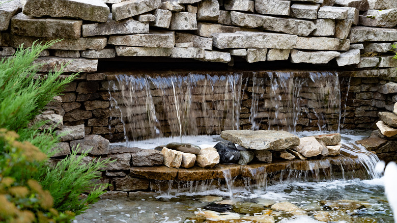A beautiful garden featuring a stone waterfall and a fountain, situated in front of a building with red canopies