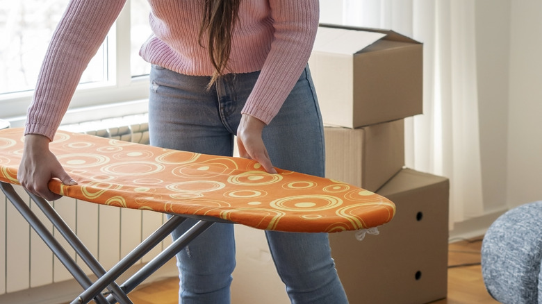 Woman picking up orange ironing board