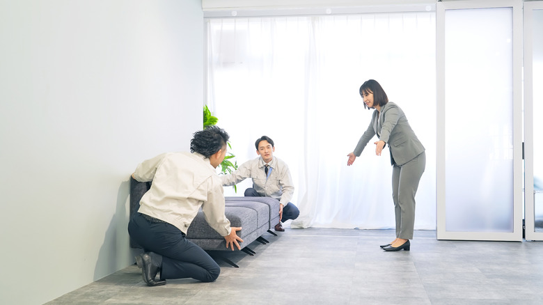 A woman showing two men where to set a sofa.