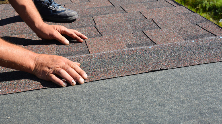 A person placing new asphalt shingles on a roof
