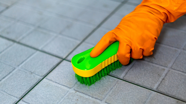 Hand with orange glove scrubbing tile with green scrub brush