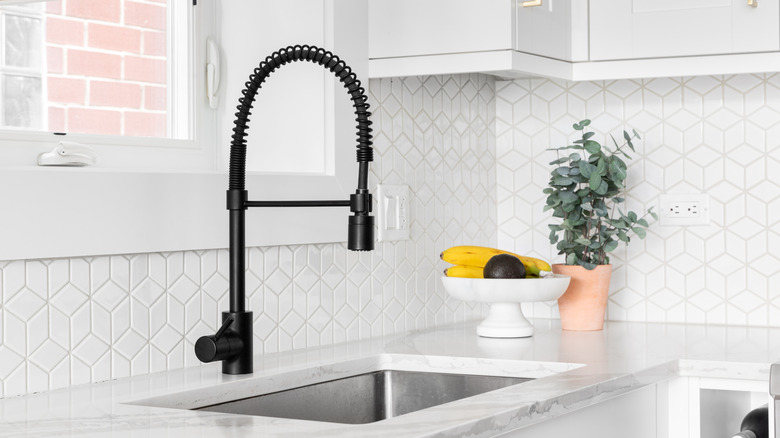 A black commercial faucet in front of a white geometric tile.