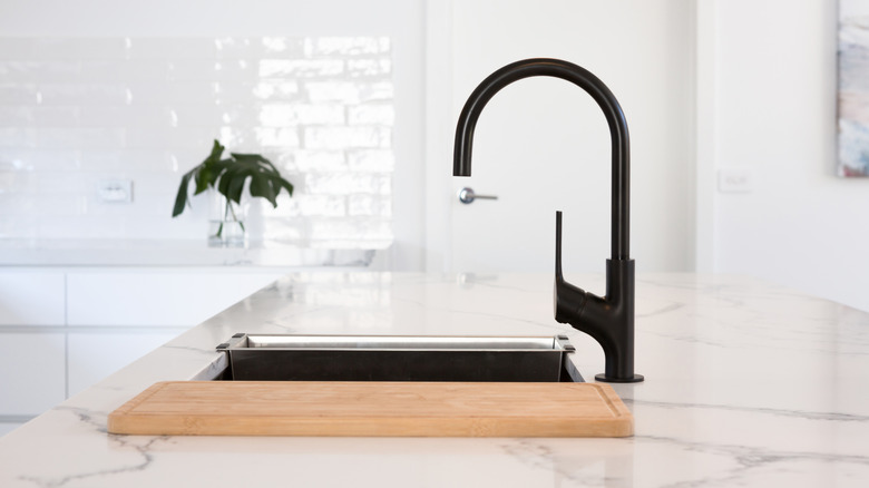 A matte black faucet against a white background with a wood cutting board in the foreground.
