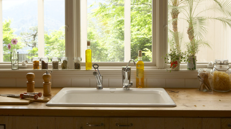 A kitchen counter next to a sink with spices, oils, jars of peppers, and salt and pepper grinders around the sink