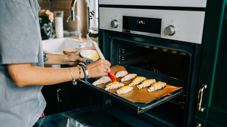 A person basting croissants and putting them in the oven