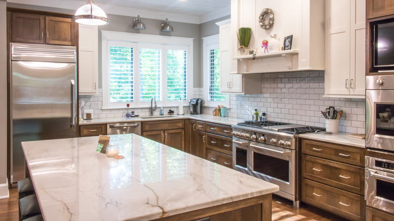 A contemporary kitchen with brown and white cabinets, a marble island, and built-in appliances