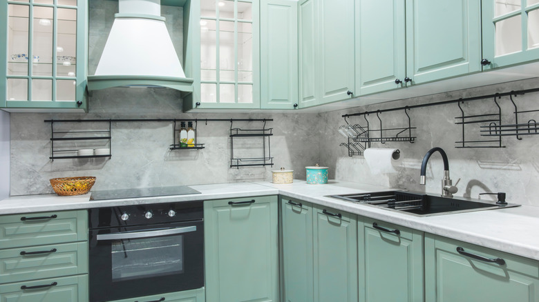 A modern kitchen with green cabinets and gray-ish backsplash