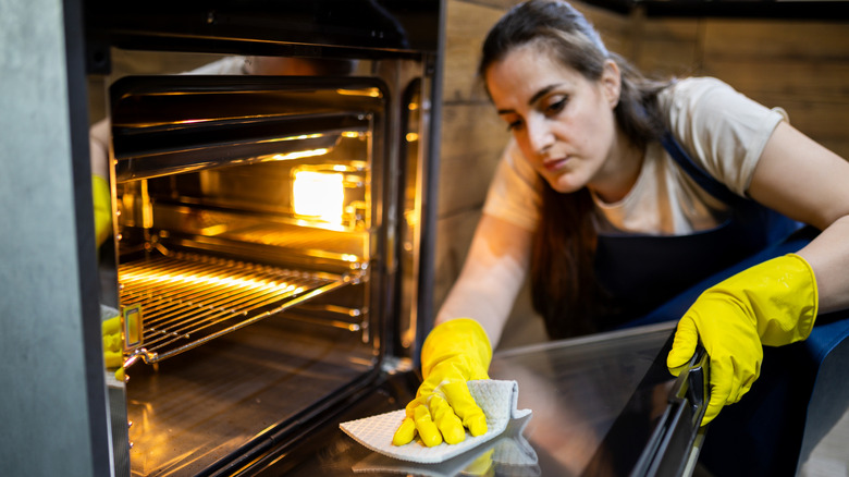 A person wearing yellow gloves, cleaning an oven door