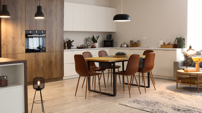 Dining table and chairs in the middle of an open concept room with kitchen along one wall.