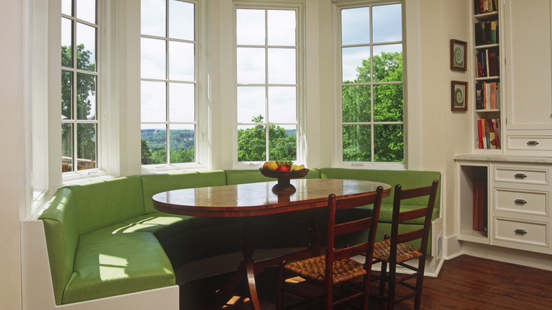 Green banquette seating with oval table and two cane chairs in front of bay window.