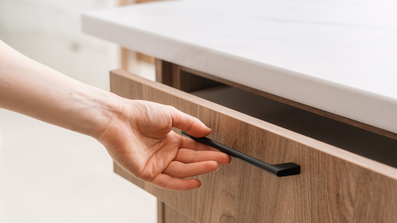 Hand opening a wood-textured kitchen drawer