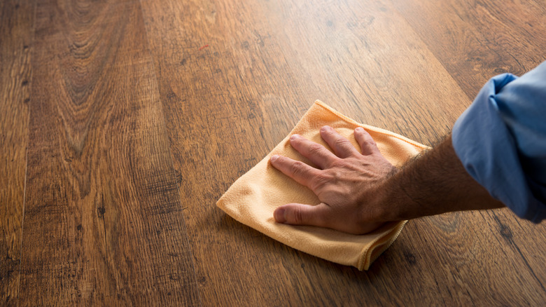 A person buffs scratches out of their hardwood floor using a soft cloth.