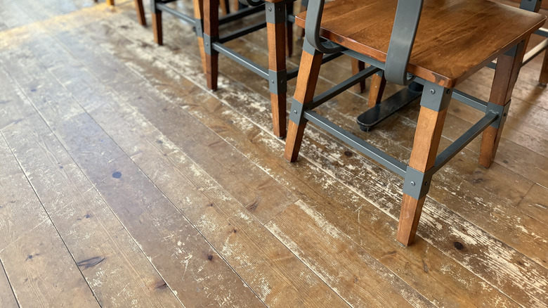 A scratched hardwood floor with dining chairs on it.
