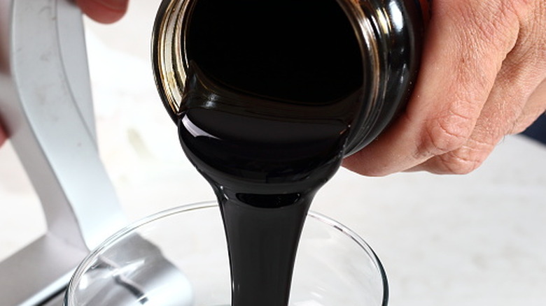 A hand pouring thick molasses into a pyrex round dish.