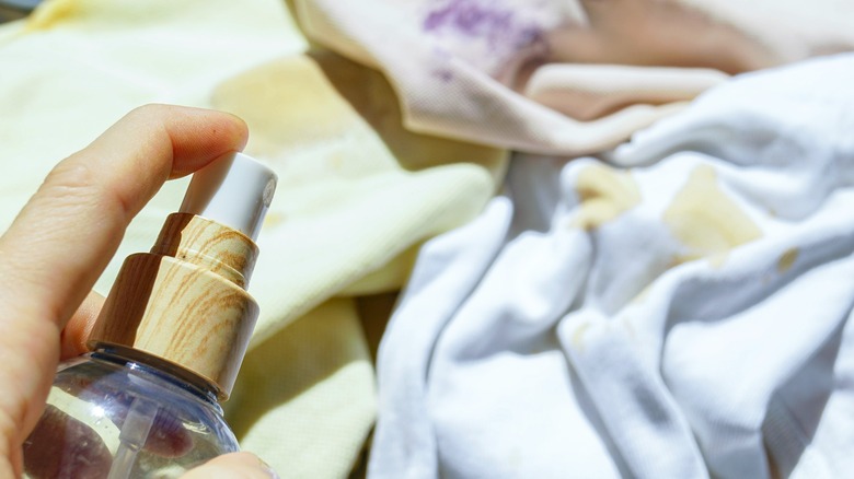 A person holds a spray bottle filled with vinegar above some stained kitchen curtains.