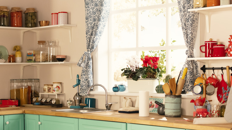 A kitchen with sage green cabinets and patterned curtains hanging in the window.