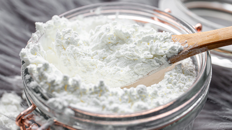 Cornstarch is scooped from a glass jar using a wooden spoon