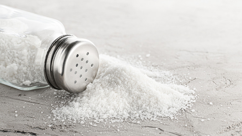 A salt shaker spilt over with a pile of salt surrounding it.