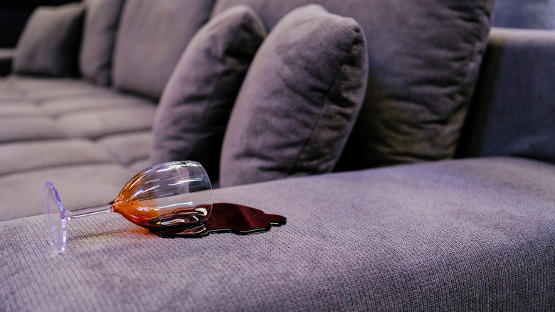 Red wine spilled on the arm of a grey couch.