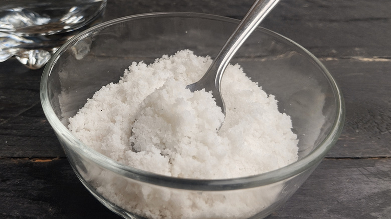 Closeup of Epsom salt, magnesium sulfate, in a glass bowl with a silver spoon dipped in