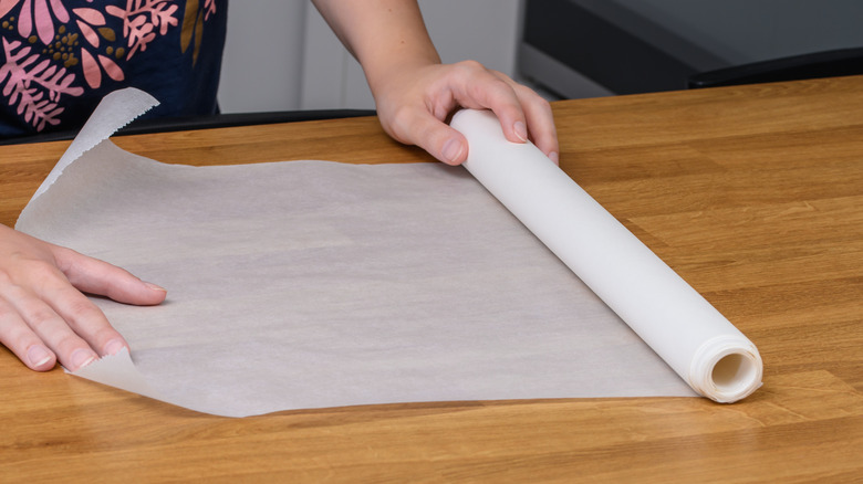 A person unrolls white wax paper on a wooden countertop