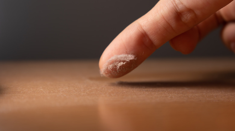 A person checks the dust on a wooden surface using their finger