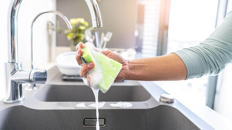 A person holds a soapy sponge under a faucet