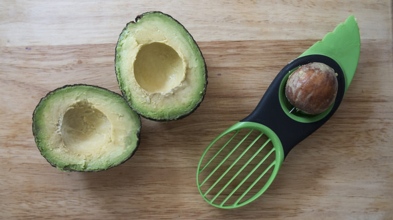 An avocado slicer next to an avocado.