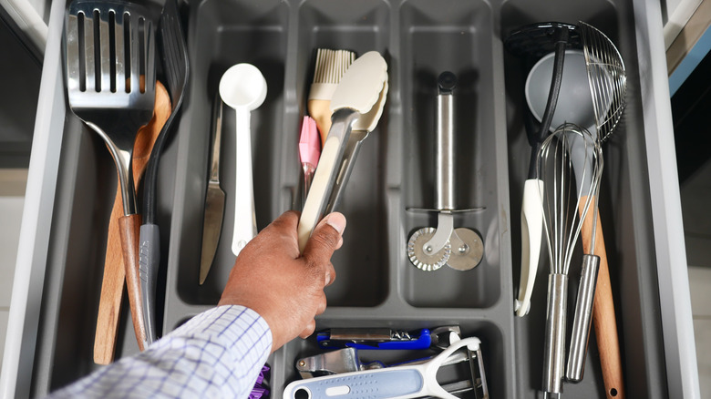 A person reaches into a utensil drawer in a kitchen.