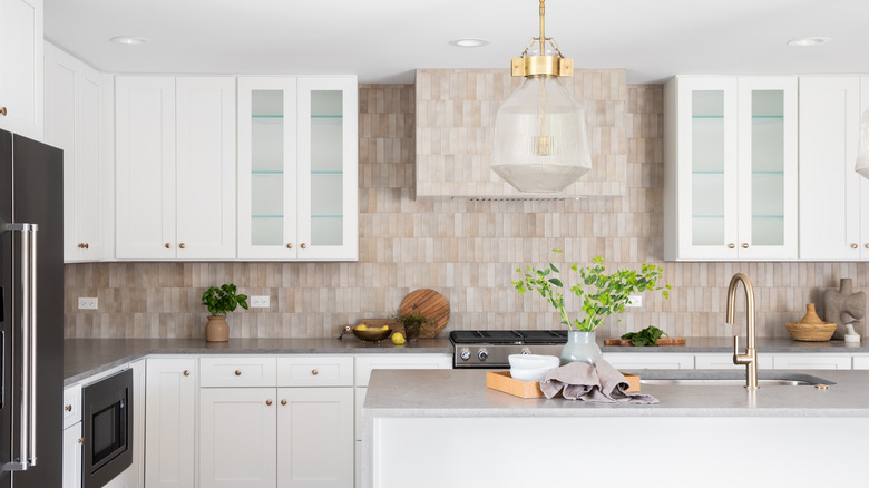 kitchen with grey stone countertop island, gold faucet, stainless steel appliances, brown tile backsplash, and white cabinets